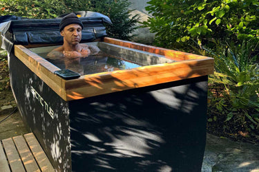 Daniel Aminati sitzt in einem Mammut-Eisbad-Behälter im Freien, umgeben von Grün. Ideal für Eisbäder, Kältetherapie und Outdoor-Kälteanwendungen.