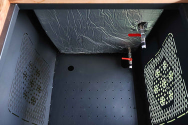 Innenansicht eines rechteckigen Eisbad-Behälters (Mammut Tub) mit silberner Isolierung an der Wand, roten Absperrhähnen und perforiertem Boden. Ideal für Eisbäder, Kältetherapie und Outdoor-Kälteanwendungen.